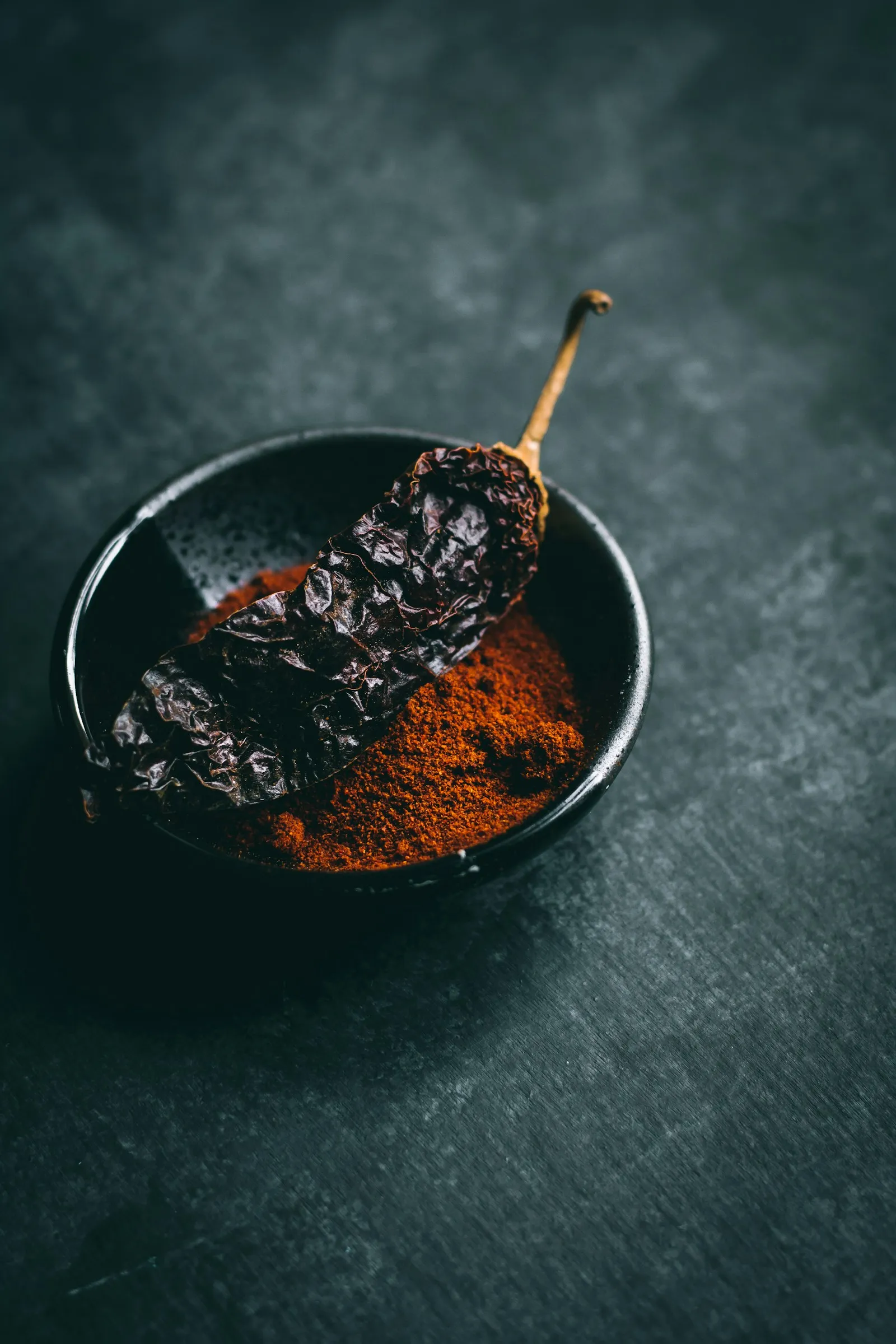 Dried chili in a black bowl next to chili powder