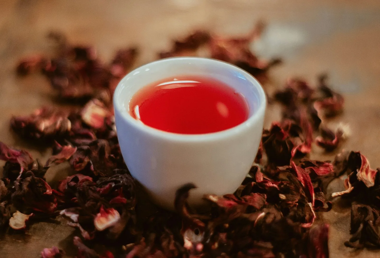 A cup of hibiscus tea surrounded by dried hibiscus flowers